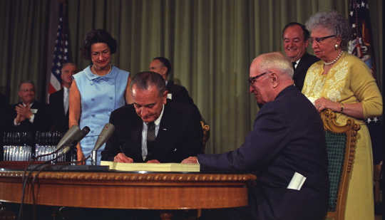 President Lyndon B. Johnson signs the Medicare Bill. President Harry S. Truman is seated next to him. LBJ Library