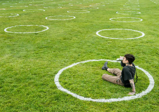 A man sits in a circle drawn in chalk in a park, sipping a beer.