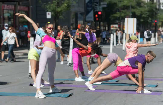People in lycra, some of it hot pink, do yoga and stretches on asphalt.