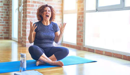 woman sitting on a yoga mat with hands up in frustration and screaming