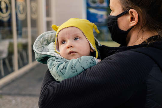 a woman wearing a surgical mask, holding a baby