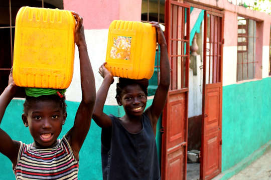 Two joyful African children carrying buckets of water on their head