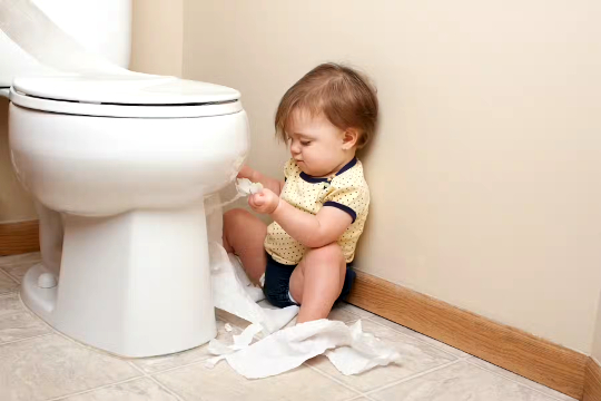 child sitting on the floor in the bathroom unrolling the toilet paper