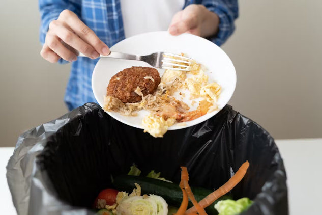 A person pours wasted food into a garbage bin.