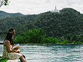 a couple sitting on the edge of a lake reading a book