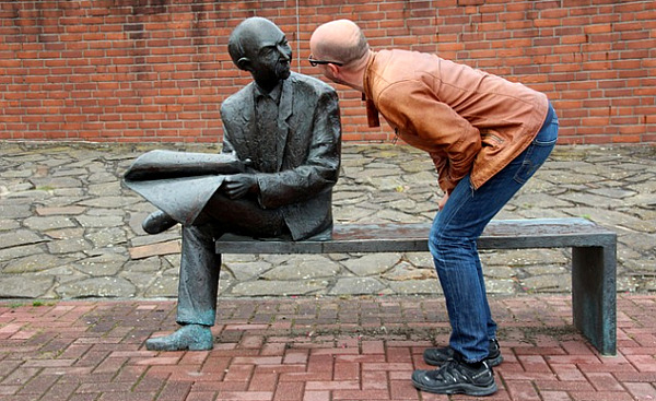 a man bending down to look closely at a sculpture on a bench