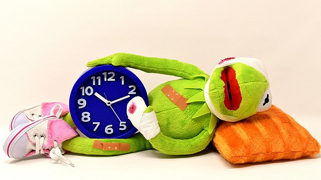 a sick frog laying down holding an alarm clock