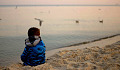 a child sitting on a beach calmly watching flying birds