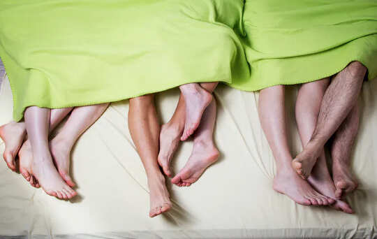 The bare feet and lower legs of three couples laying under the same lime green blanket. 