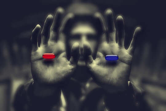 man in shadows holding out a red pill in one hand and a blue pill in the other