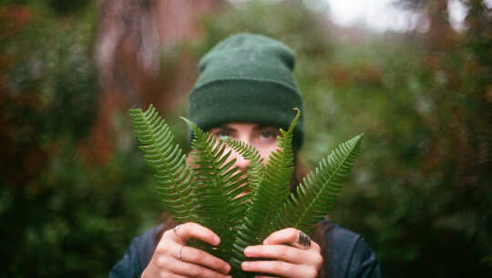 a young man holding some ferns and using them to hide behind