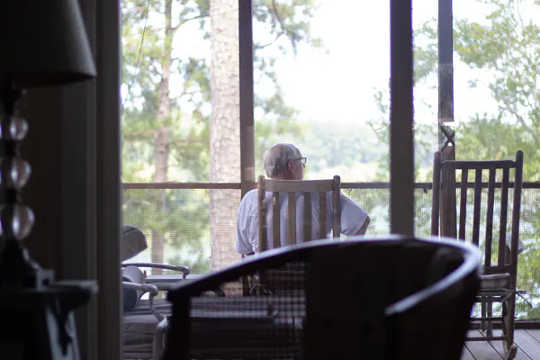 Man sits on chair on balcony looking out at woods