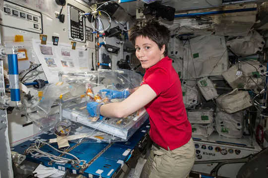 Woman in zero gravity conducting experiment, surrounded by equipment.
