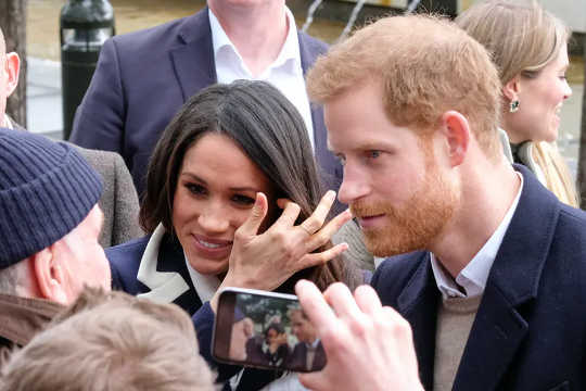 Harry and Meghan are photographed on a smartphone while speaking to a crowd