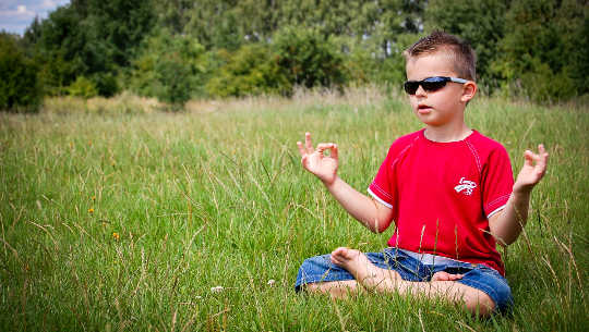 young boy wearing sunglasses meditating in an open field