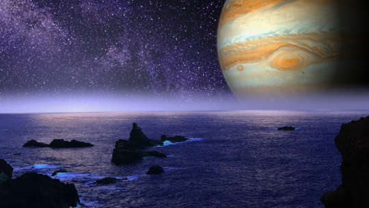 image of the planet Jupiter on the skyline of a rocky ocean shore