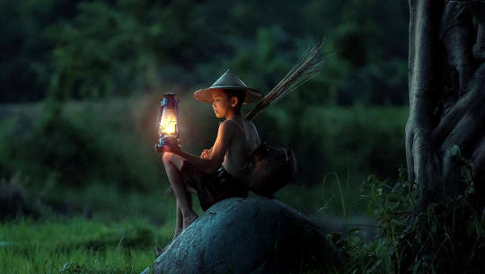 young boy sitting outside with a lantern, waiting for dawn
