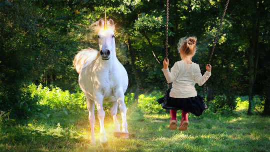 young girl on a swing looking at a unicorn
