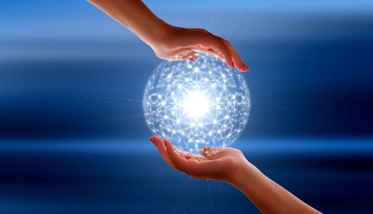 two people's hands holding a globe made of connecting points of light