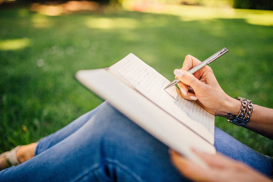 a person sitting outside on the grass writing in a notebook