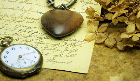 a pocket watch and a heart pendant laying on top of a handwritten letter