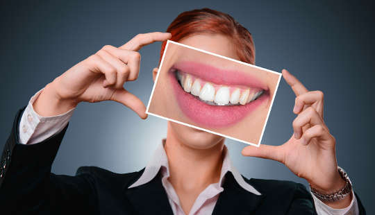 a woman holding up an enlarged photo of her teeth