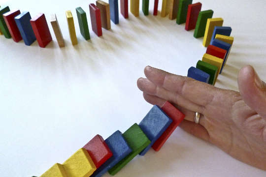 a hand holding back a barricade of dominoes from falling