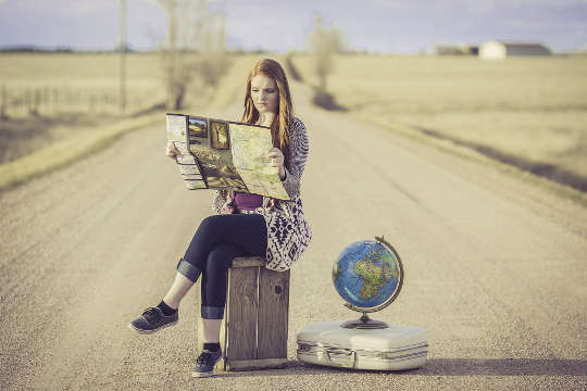 a young woman sitting on a suitcase in the middle of the road with a globe of planet earth next to her