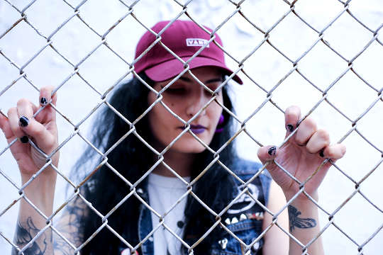 girl wearing a baseball cap standing behind a chain link fence