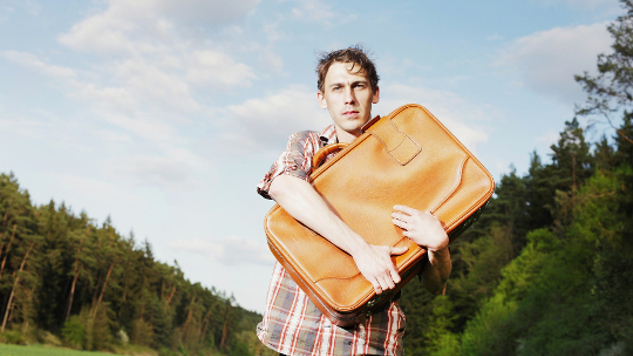 man standing outside clutching a suitcase to his chest
