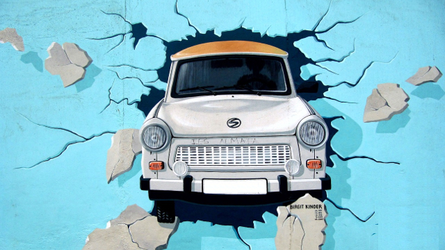 old car bursting through a blue paper wall