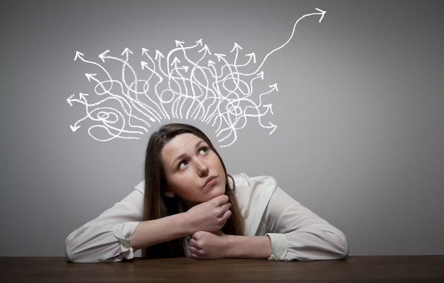 Girl thinking with arms resting on a table, arrows in different directions above her head