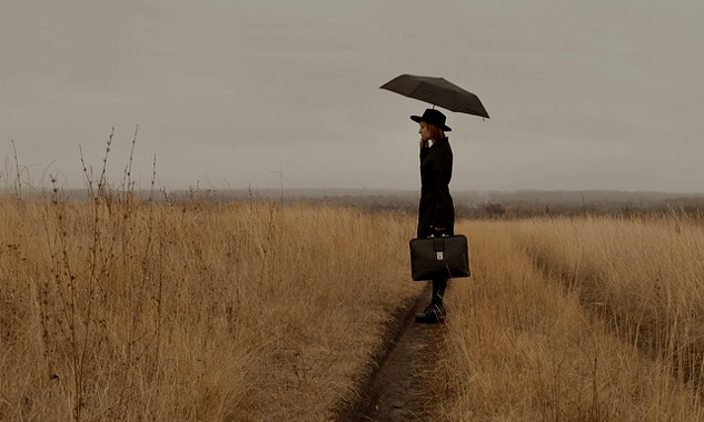 image of a woman on a trail in an open field and holding a suitcase