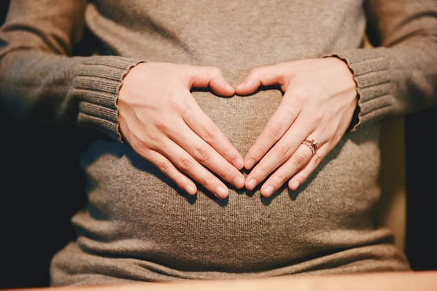 woman's hands forming a heart shape on top of her womb