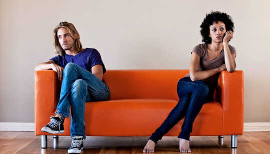 A couple sits on opposite sides of an orange couch looking away from each other