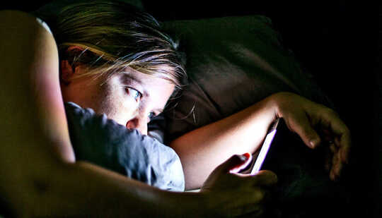 A woman in bed reads her phone