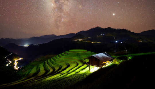 bright light from under small building light terraced rice fields under starry sky