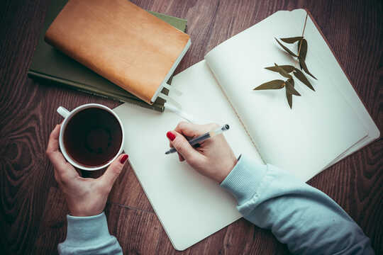 person writing in a notebook holding a cup of coffee