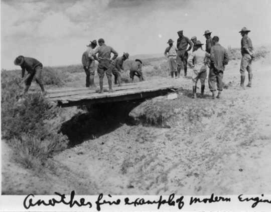 Soldiers assess a plank bridge over a gully.