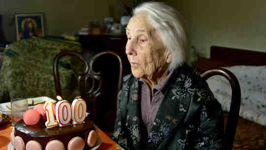 A 100-year-old woman blows out the candles on her birthday cake.