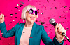 grey-haired woman wearing funky pink sunglasses singing holding a microphone