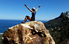 hiker sitting on top of a huge rock with arms up in the air in triumph