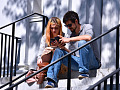 a couple sitting on some outside stairs looking at their phones