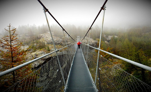 a rope bridge over a chasm with one person in the middle of the bridge