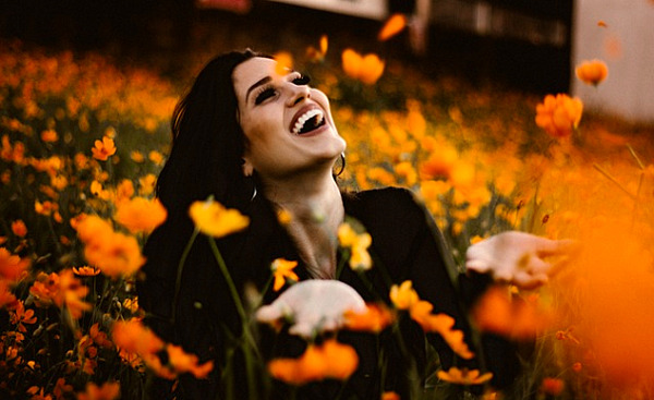 زنی که در مزرعه ای از گل های نارنجی روشن می خندد