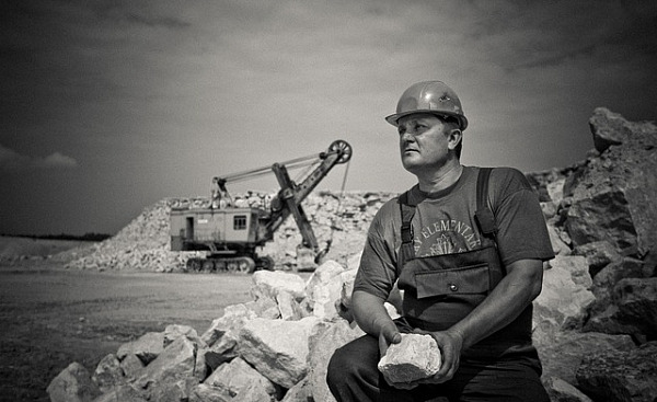 man sitting holding a big rock on a construction site