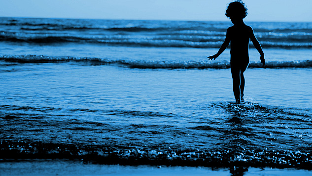 ung pojke som står i vattnet vid kanten av vågorna som porlar in