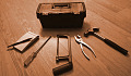 tookbox with 5 tools spread out around it: notepad, screwdriver, hacksaw, pliers, hammer