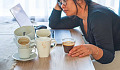 a woman looking stressed and tired drinking a cup of coffee and surrounded by multiple cups empty and full
