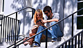 a couple sitting on some outside stairs looking at their phones